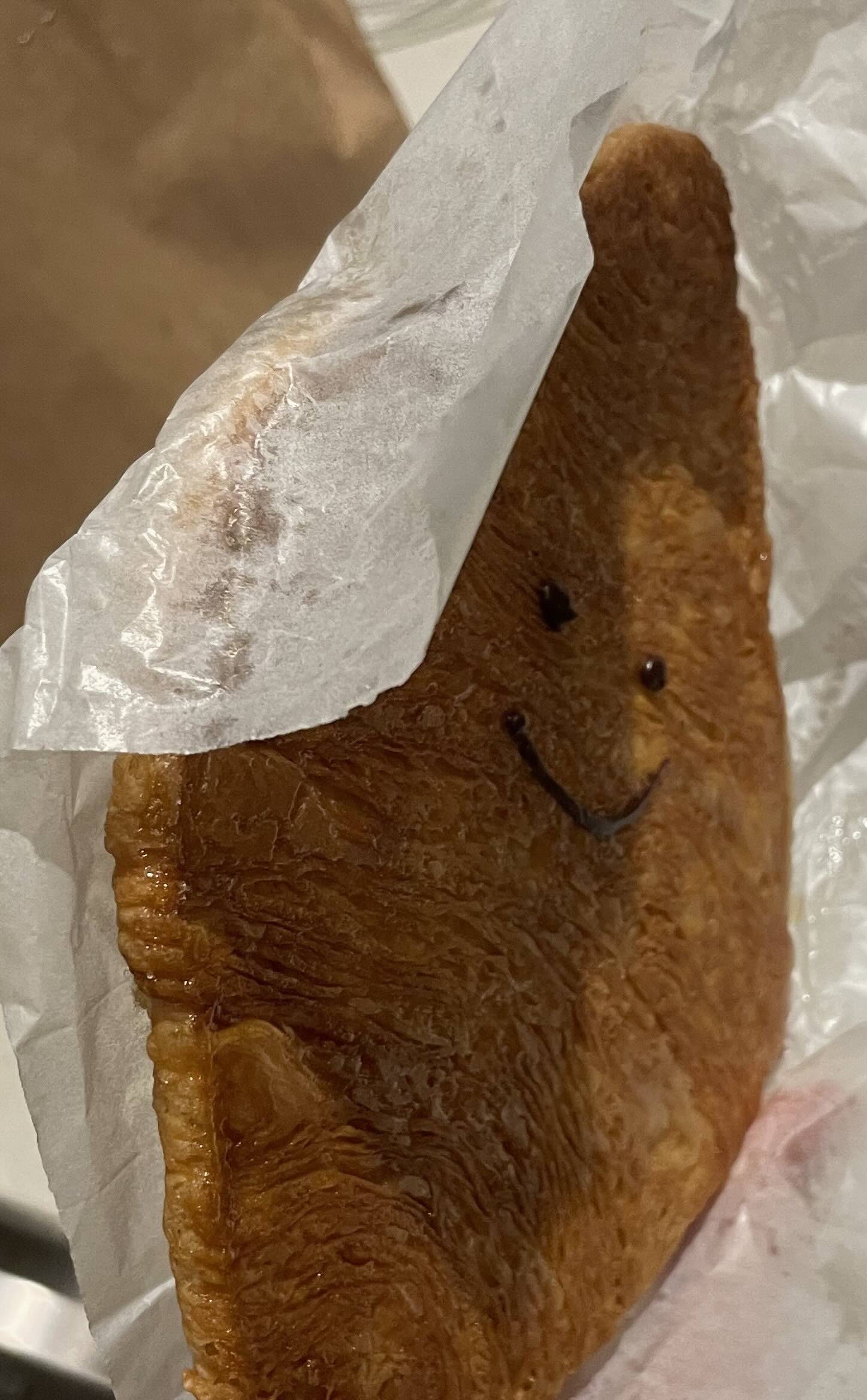 A flattened croissant with a chocolate drizzle that looks like a smiley face